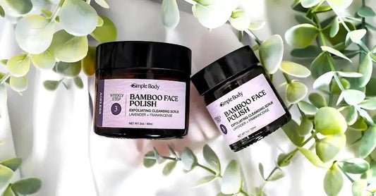 A photo of Simple Body Bamboo Face Polish in Lavender + Frankincense sitting on a white cloth with plants around it.