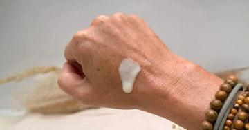A photo of a hand with Simple Body's Barrier Defense Serum on it dripping down the hand with wooden beaded bracelets on the wrist and a blurred background.