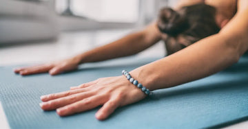 A photo of a woman on a yoga matt doing child's pose with a blue beaded bracelet.