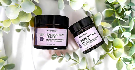A photo of Simple Body Bamboo Face Polish in Lavender + Frankincense sitting on a white cloth with plants around it.