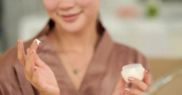 A photo of the bottom half of the face of a young lady in a beige robe showing she just dipped her finger in Simple Body Face Cream.