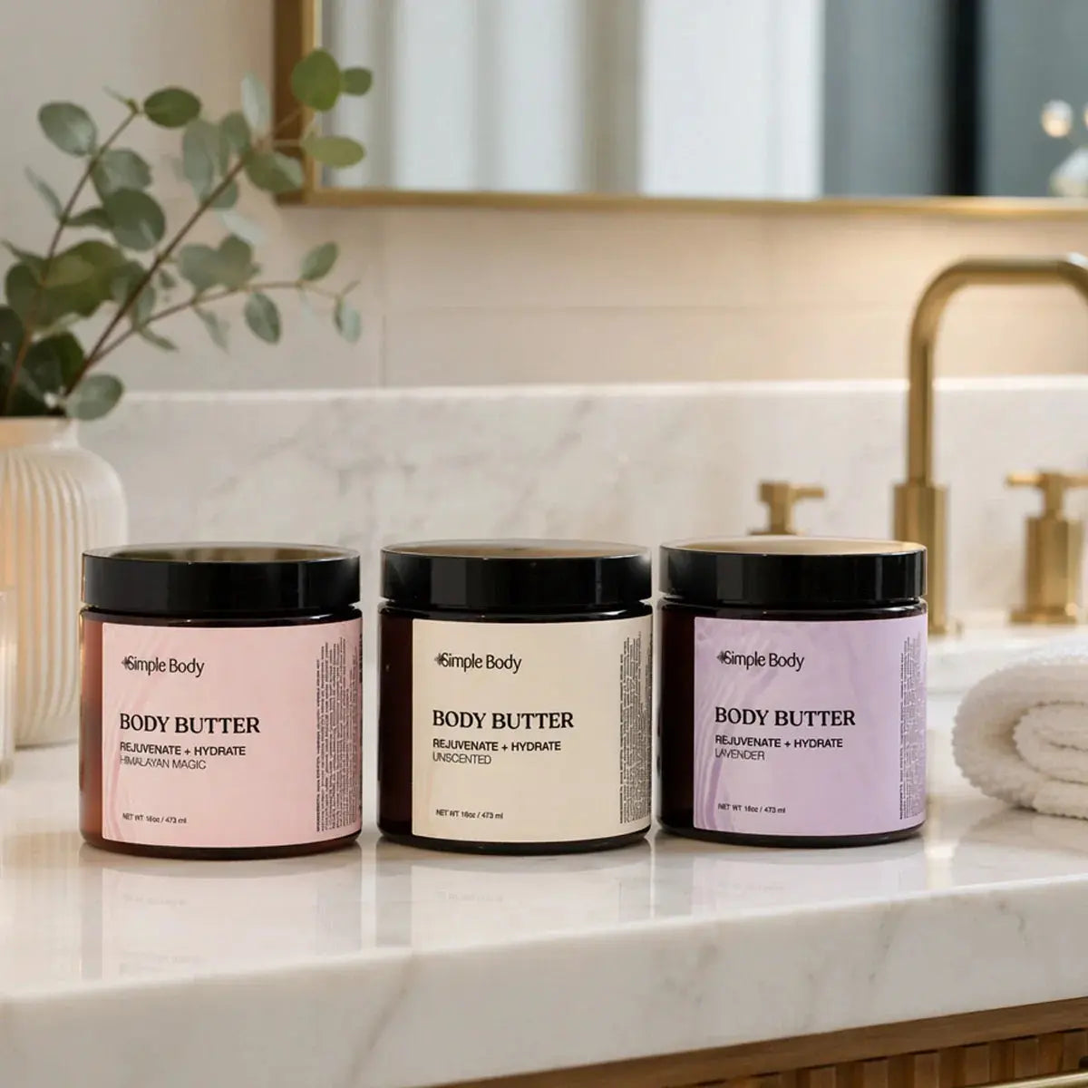 A collection of three scented body butters from Simple Body including Himalayan Magic, Unscented and Lavender sitting on a modern bathroom countertop.