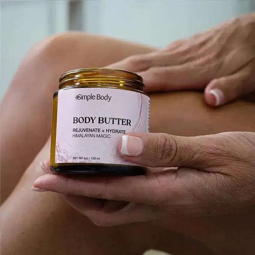 A photo of a bare leg and hands applying Simple Body Body Butter in Himalayan Magic with a blurred background.