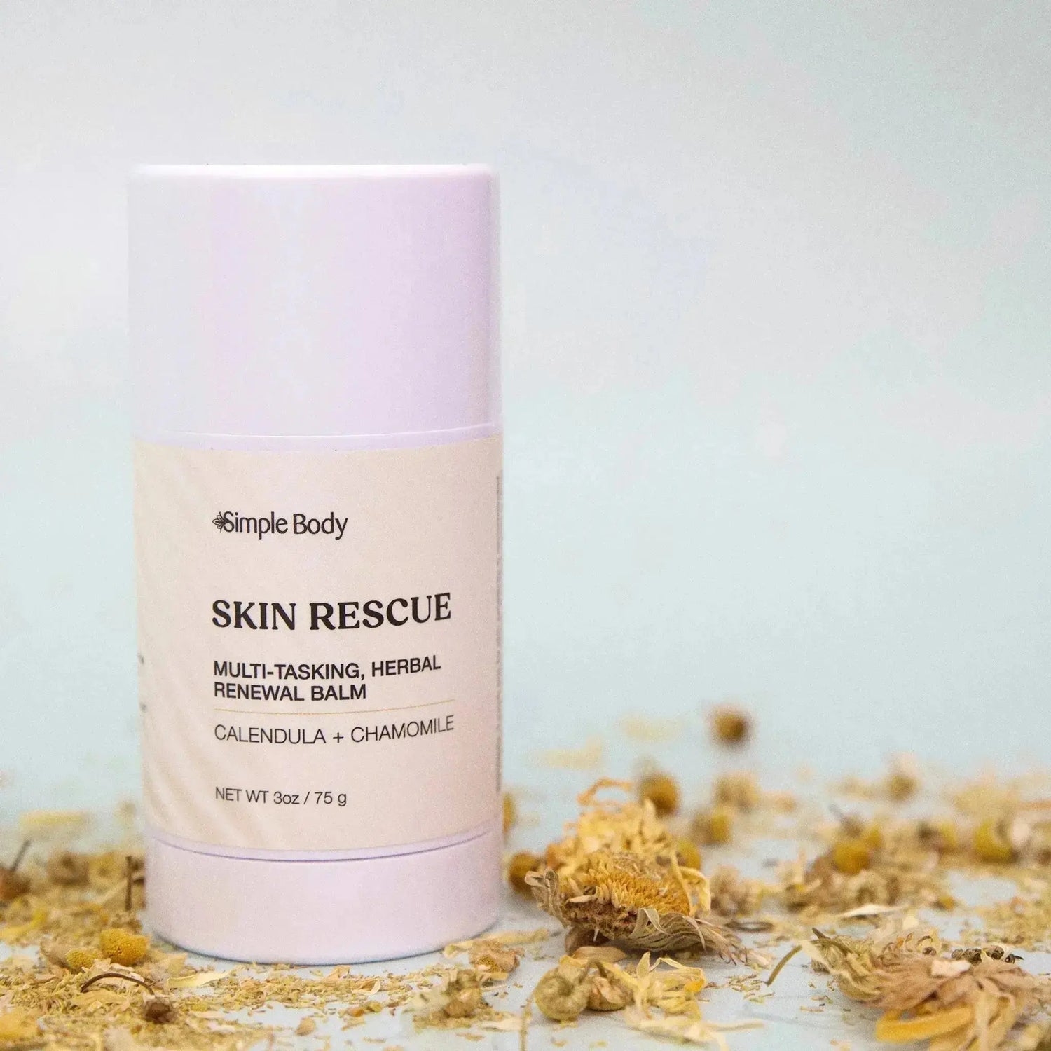 A twist up tube of Simple Body Skin Rescue multi-tasking herbal balm is surrounded by calendula petals on a light green background