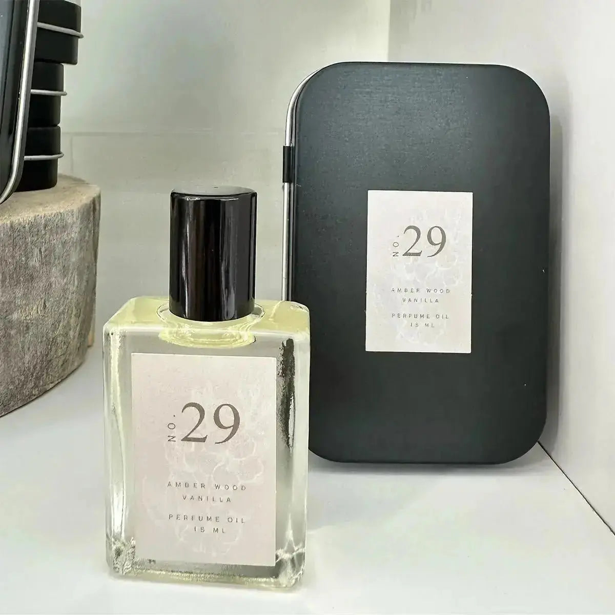 A photo of a no. 29 natural essential oil perfume roller in a glass bottle with a black top and a black tin behind it on a white background.