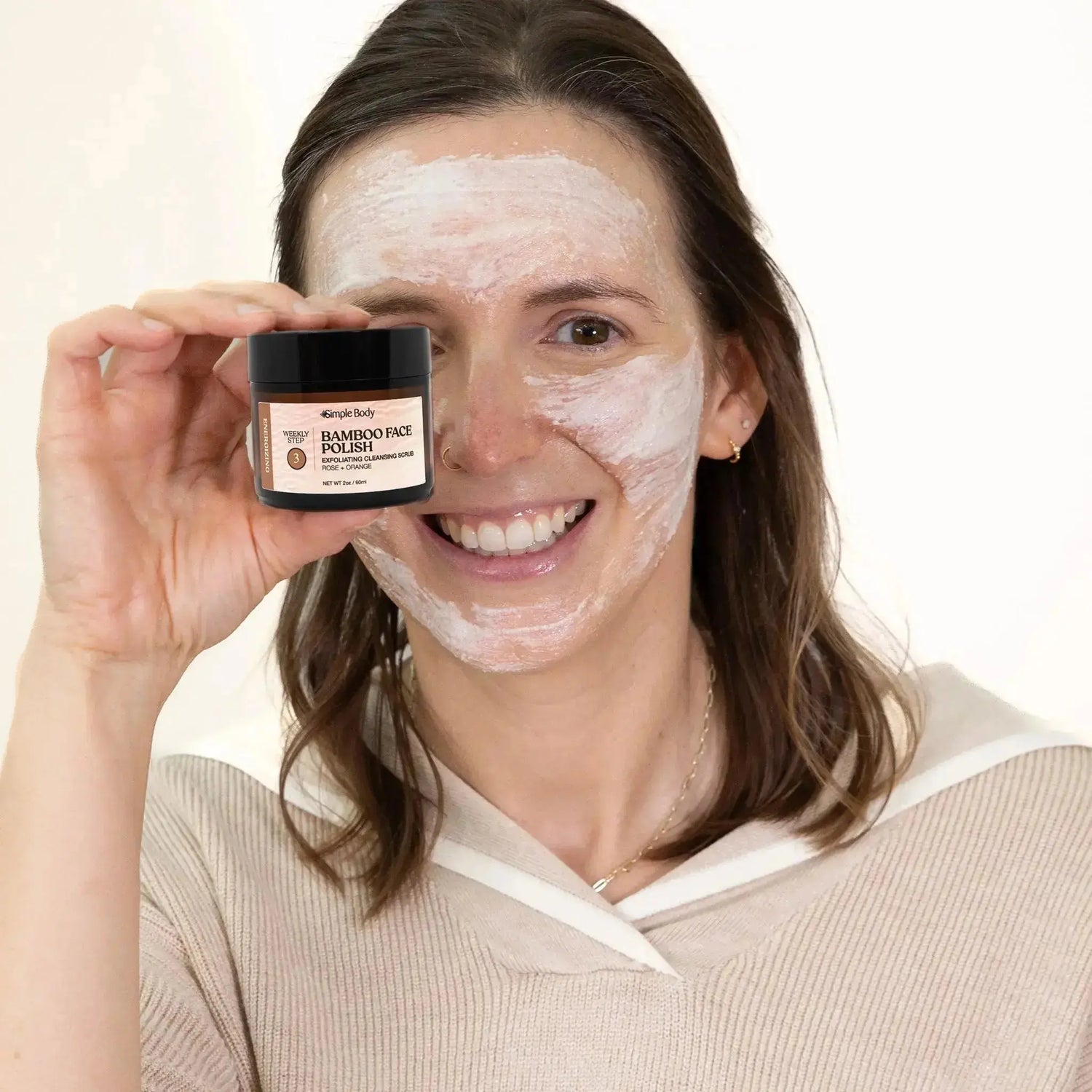 Ashley is holding a jar of Simple Body Bamboo Face Polish, an exfoliator scrub that she has on her face.