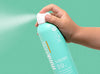 Hand holding a blue sunscreen spray bottle with a green background