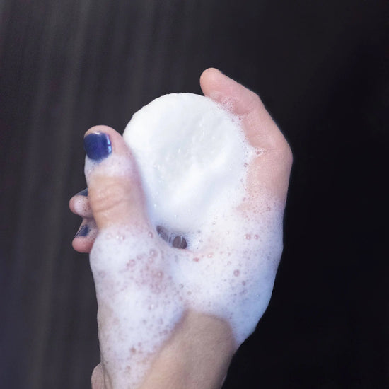 Hand holding a foamy shampoo bar against a dark background