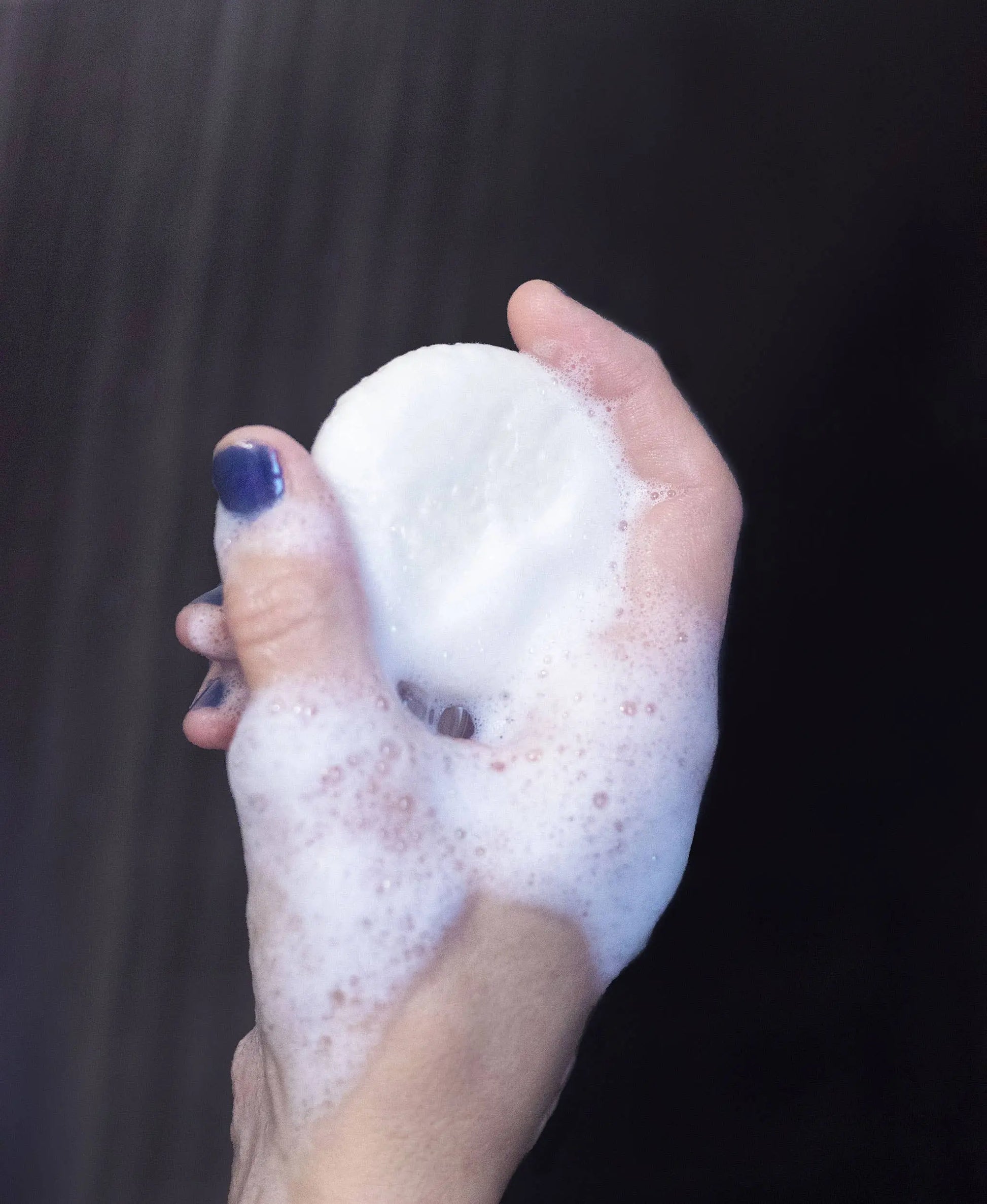 Hand holding a foamy shampoo bar against a dark background