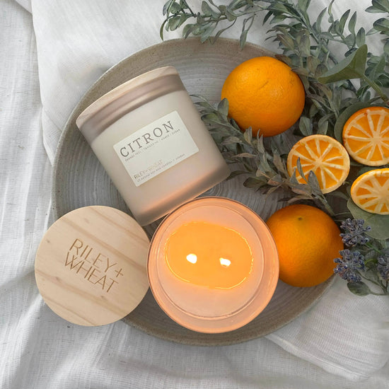 Candle labeled 'Citron' by Riley + Wheat with oranges and greenery on a neutral background