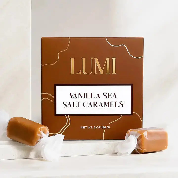 Lumi Vanilla Sea Salt Caramels in a brown box with gold accents, styled on a white marble surface with two unwrapped caramels in the foreground.