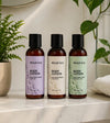 Three bottles of Simple Body lotion in a 2.5oz Travel size including Lavender, unscented and Rosemary Mint on a marble surface with plants in the background