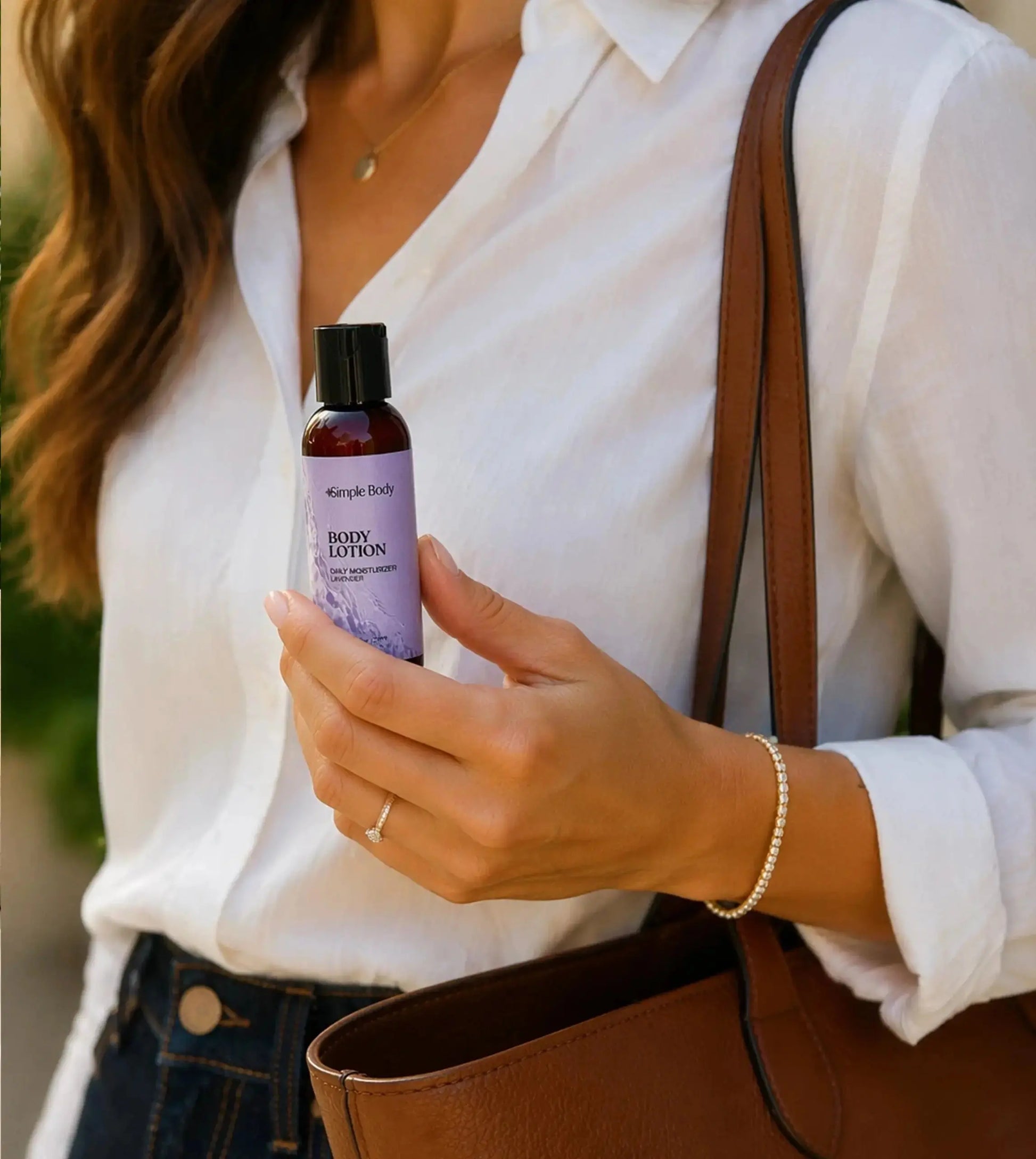Woman holding a Simple Body 2.5oz Travel Body Lotion Bottle with a brown leather bag