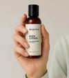 Hand holding a bottle of Simple Body Travel Lotion in Unscented and Fragrance Free against a neutral background. 
