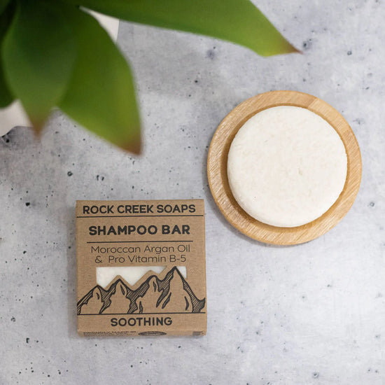 Rock Creek Soaps shampoo bar with packaging on a textured surface with a plant leaf.