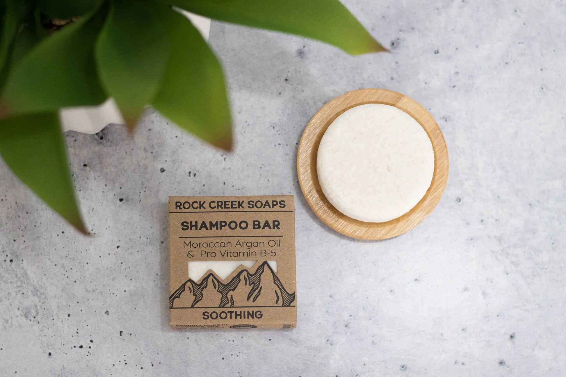 Rock Creek Soaps shampoo bar with packaging on a textured surface with a plant leaf.
