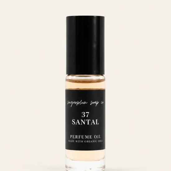 A clear glass bottle of Santal 37 perfume oil from Benjamin Soap Cowith a black cap and a black label, set against a solid off-white background.