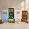 Four LUMI hot chocolate packaging boxes on a neutral background with a bowl of cacao powder and mint leaves.
