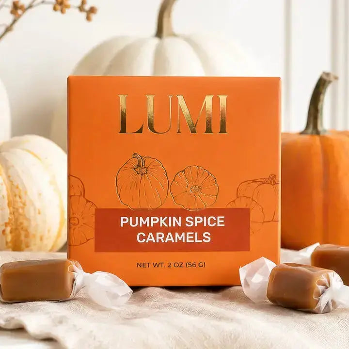 LUMI Pumpkin Spice Caramels in an orange box with gold lettering, styled with wrapped caramel candies and pumpkins on a neutral fabric surface.