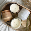 Four candles in decorative holders on a wooden tray with a brand name tag.