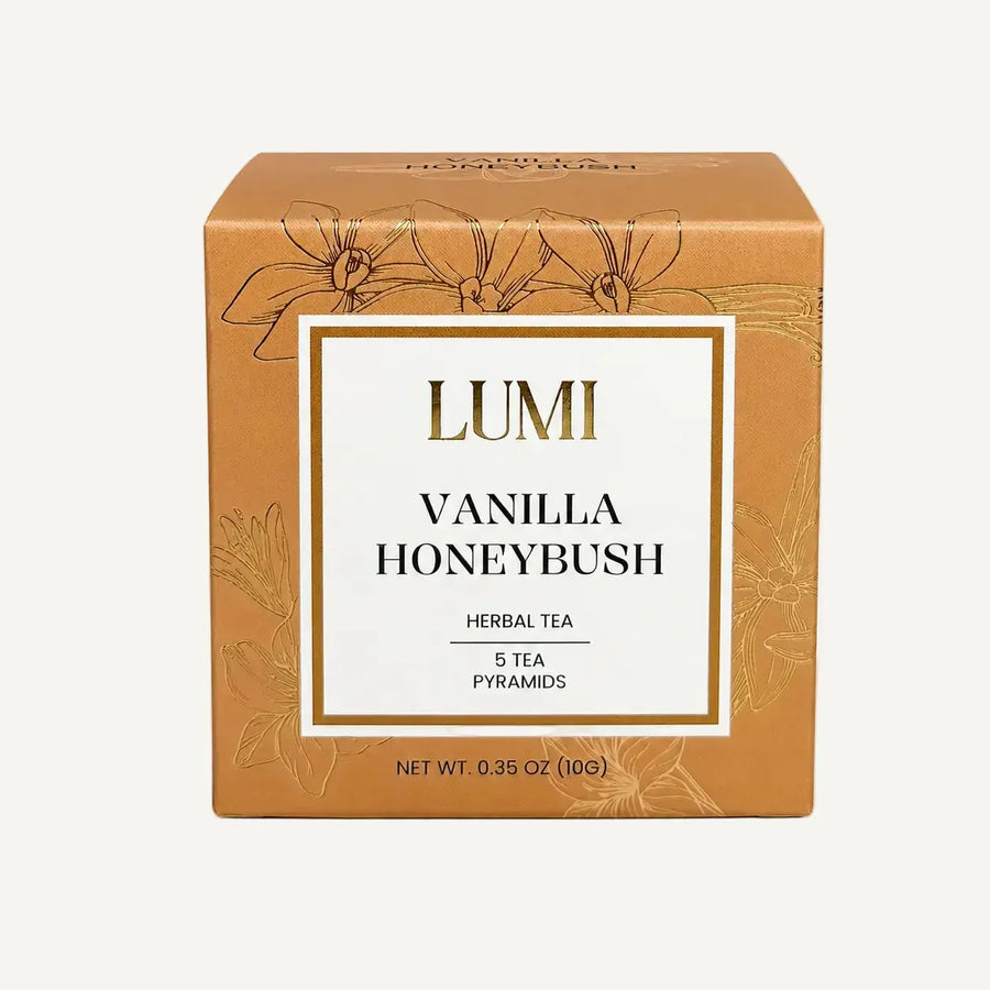 A square cardboard box of Lumi Vanilla Honeybush herbal tea, featuring a warm tan-brown color with gold floral line art and a central white label with gold and black text.