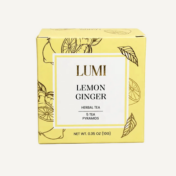 A yellow box of Lumi Lemon Ginger Herbal Tea, featuring a white central label with gold and black text, decorated with gold line drawings of lemons and leaves on a white background.