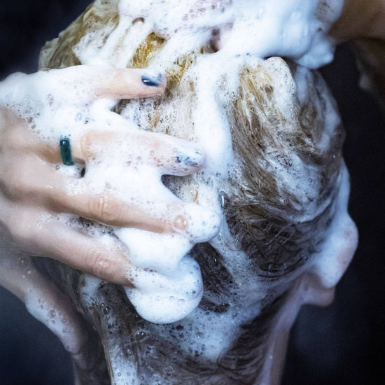 Hand scrubbing hair with a shampoo bar and soap suds against a dark background