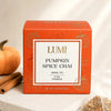 A box of Lumi Pumpkin Spice Chai herbal tea sits on a light stone surface with a small pumpkin, cinnamon sticks, and loose tea visible around it. The box is orange with a white front label and gold pumpkin illustrations.