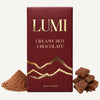 A 3 oz box of LUMI Creamy Hot Chocolate in its burgundy and gold wrapper, displayed with a pile of cocoa powder on the left and several broken chocolate pieces on the right, all on a clean white background.