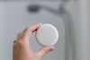 Hand holding a white round shampoo bar against a blurred background