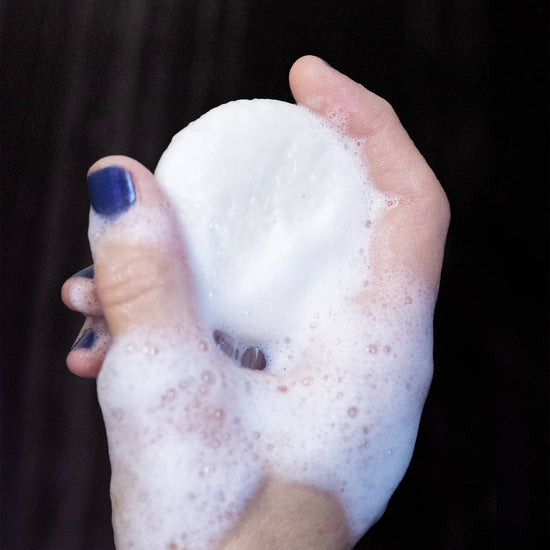 Hand holding a foamy soap bar with a dark background