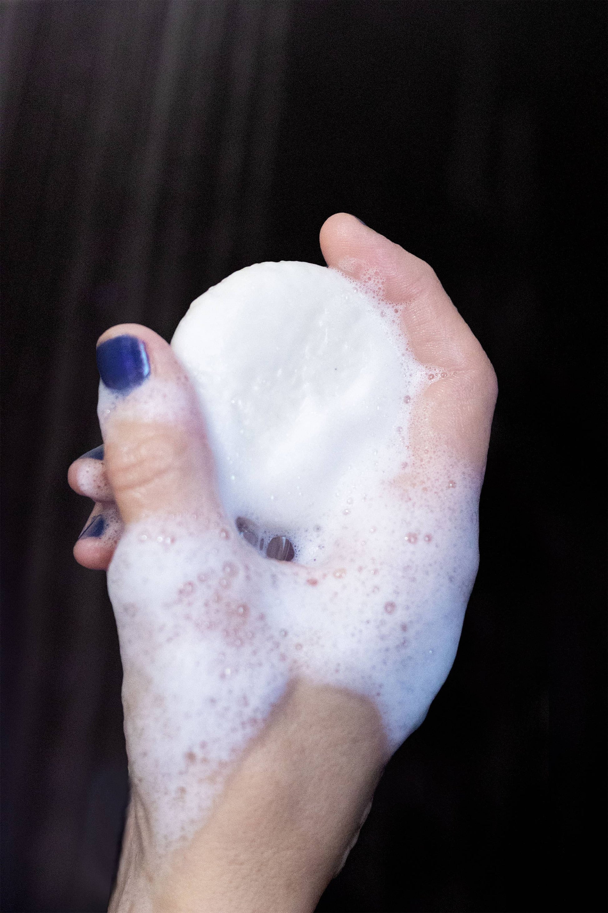 Hand holding a foamy soap bar with a dark background