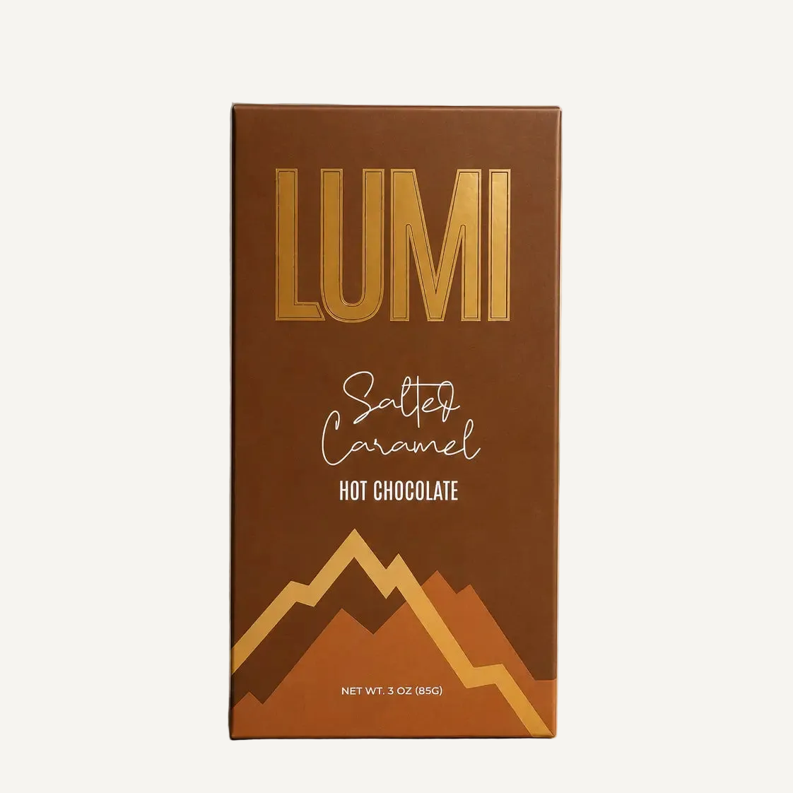 A 3 oz box of Lumi Salty Caramel Hot Chocolate, featuring a rich brown packaging design with metallic gold lettering and mountain graphics, set against a textured gray background with soft window shadows.