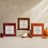 Three LUMI tea boxes arranged on a stone pedestal: Wild Cranberry in burgundy, Apple Cinnamon in brown, and Pumpkin Spice Chai in orange. The boxes are styled with cranberries, an apple slice, cinnamon sticks, and a small pumpkin on a light stone surface against a textured beige backdrop.