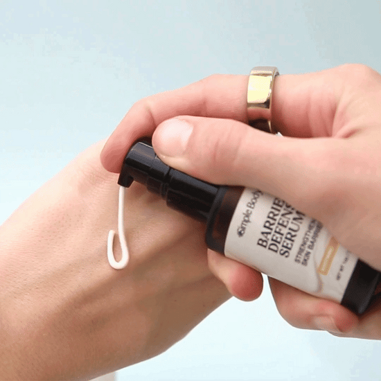 A hand applying Simple Body Barrier Defense Serum which is a creamy off-white texture