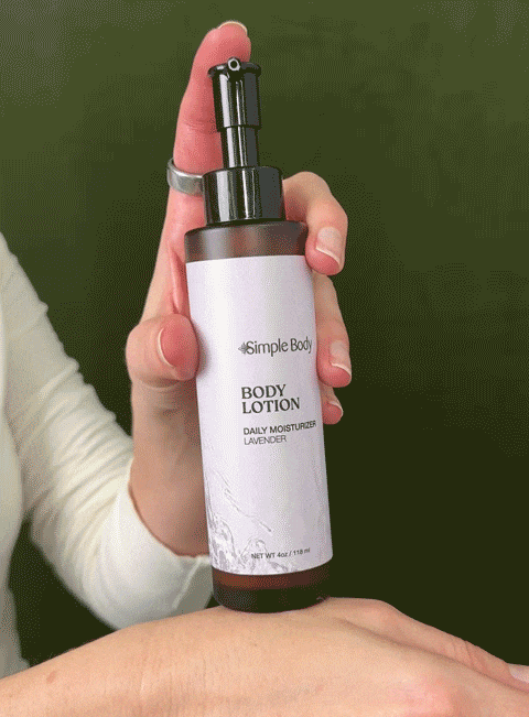 A hand pumps Simple Body Lotion which is a creamy white texture onto their hand with a green background.