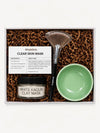 A Simple Body Clay Mask Kit with a White Kaolin Clay Mask, Green Bowl, Fan Brush and recipe card with kraft crinkle paper in a gift box.