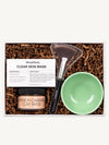 A clay mask gift set including a caramel clay mask, recipe card, green bowl and fan brush with kraft crinkle paper in a gift box.