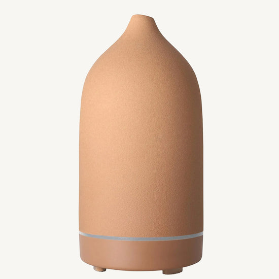A modern ceramic essential oil diffuser in an earthy rust color against a white background.