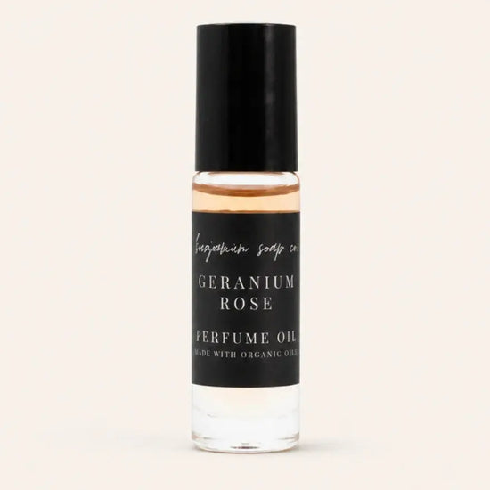 A small cylindrical bottle of Geranium Rose Perfume Oil by Benjamin Soap Co, featuring a black cap and a black label with white text, set against a solid off-white background.