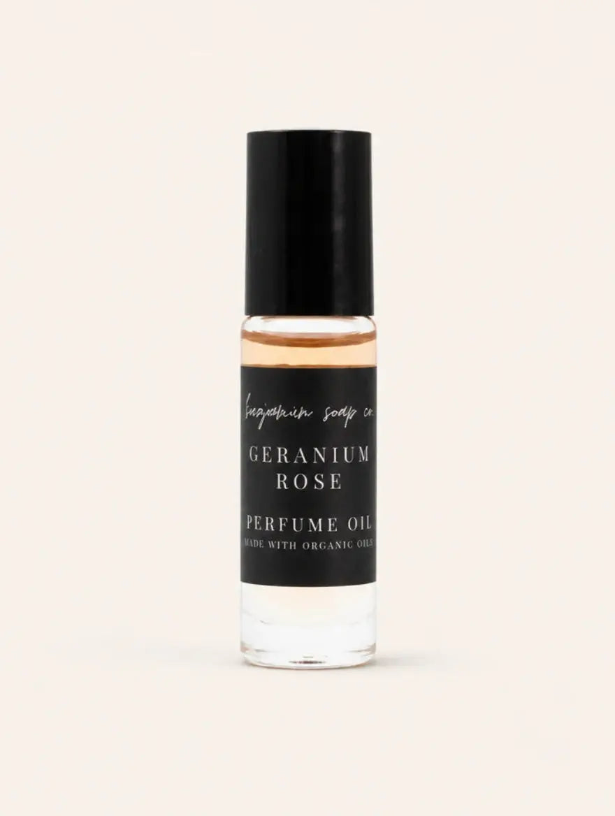 A small cylindrical bottle of Geranium Rose Perfume Oil by Benjamin Soap Co, featuring a black cap and a black label with white text, set against a solid off-white background.