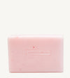 A handmade bar of soap with a pink color and an embossed Simple Body design on it, placed against a tan background.