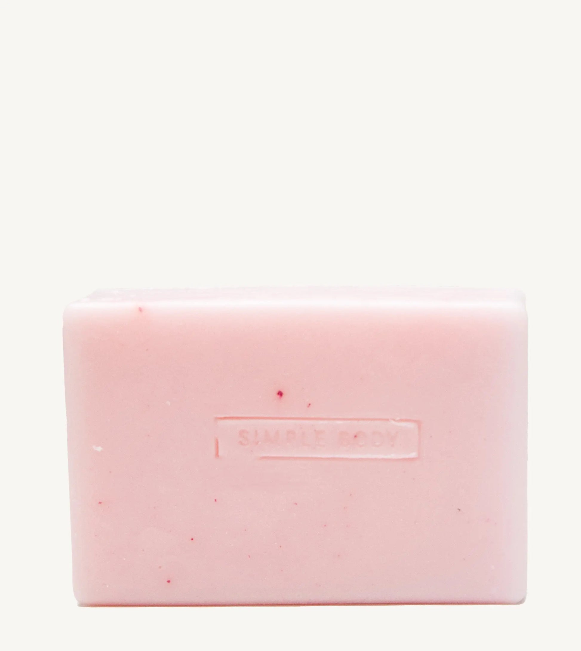 A handmade bar of soap with a pink color and an embossed Simple Body design on it, placed against a tan background.