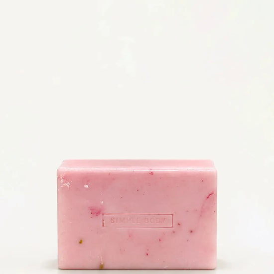 A handmade bar of soap with a pink color and an embossed Simple Body design on it, placed against a tan background.