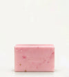 A handmade bar of soap with a pink color and an embossed Simple Body design on it, placed against a tan background.