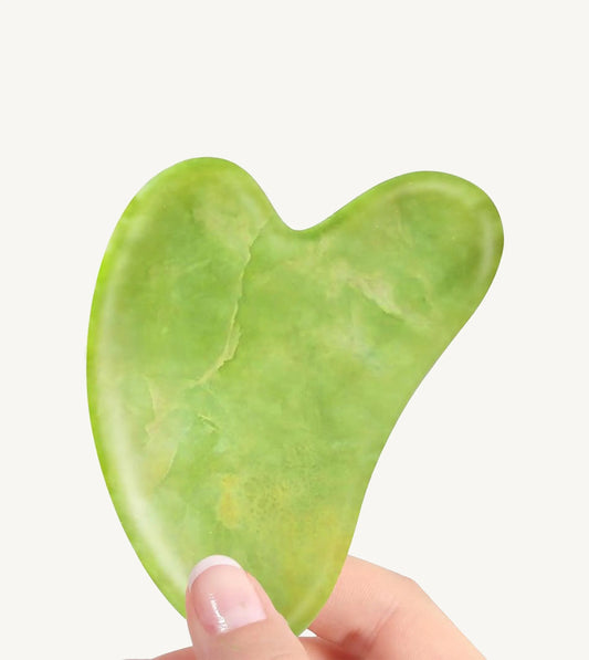 Two fingers holding a green Jade Gua Sha tool on a white background.