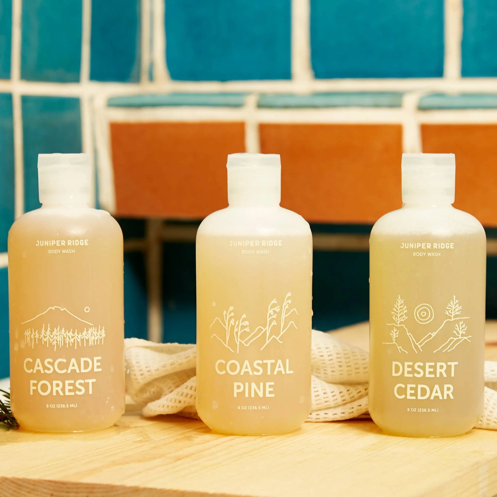 Three bottles of Juniper Ridge body wash with different scents on a wooden surface.