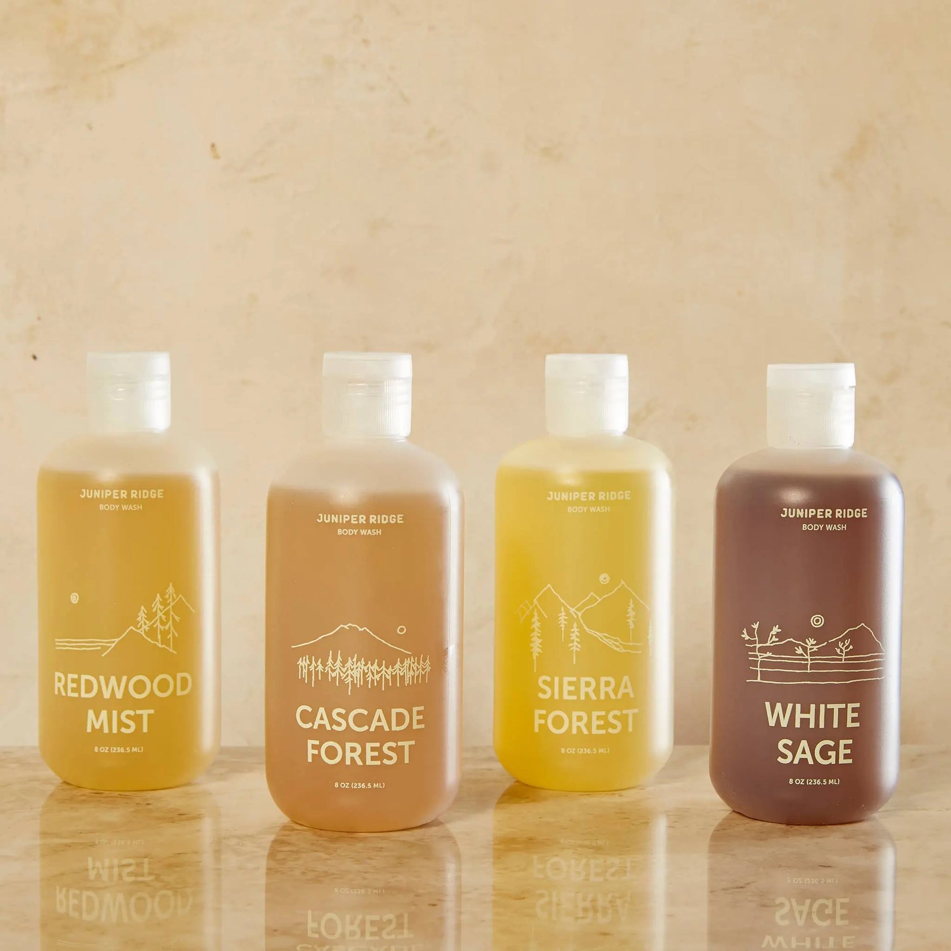 Four bottles of Juniper Ridge body wash on a wooden surface with a beige background