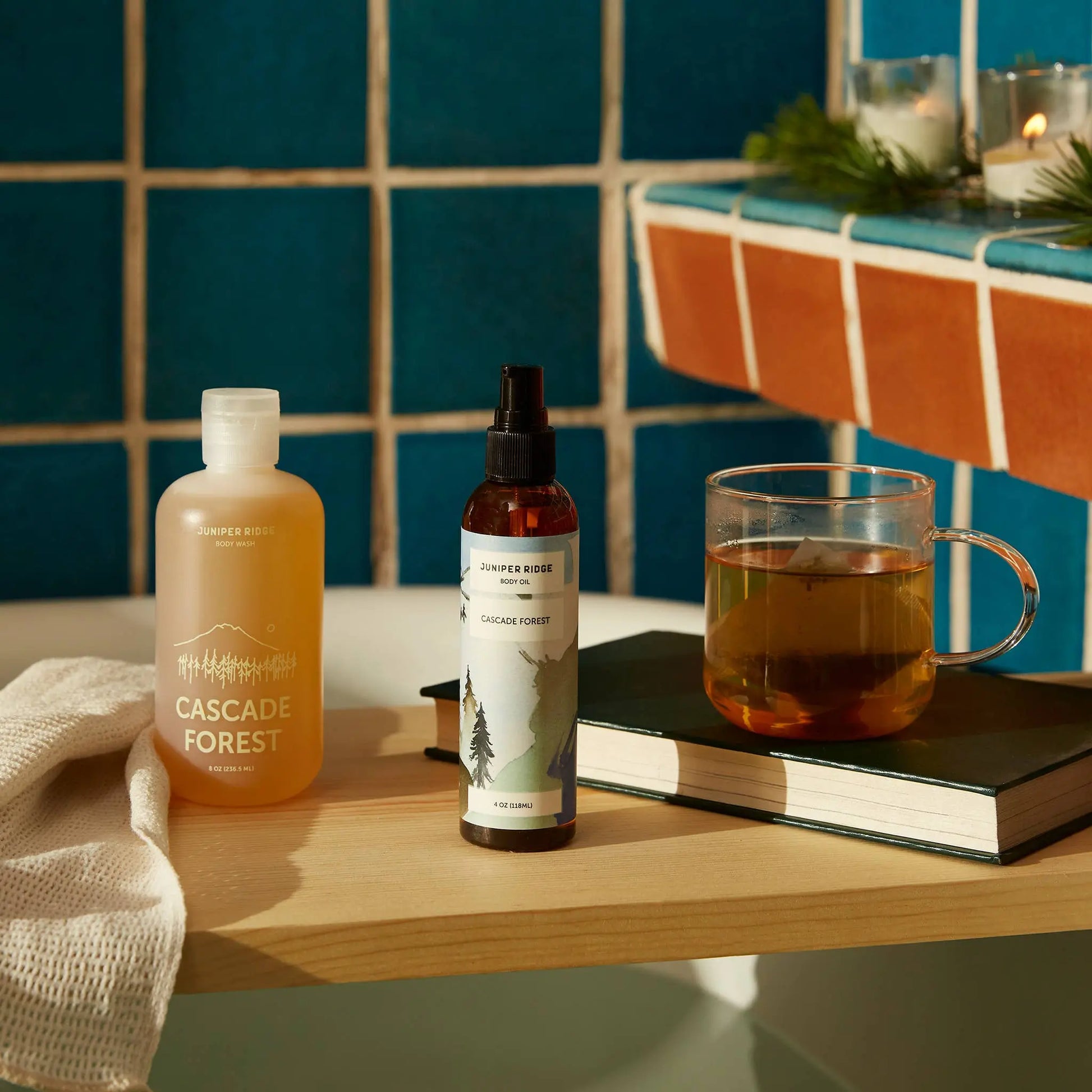 Juniper Ridge Body Wash in Cascade Forest and Juniper Ridge Body Oil in Cascade Forest sitting next to a glass mug of tea in a warm, rustic bathroom setting.