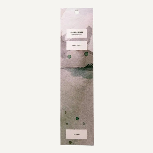 A tall, narrow package of Juniper Ridge Campfire Incense in Sweetgrass with a watercolor-style abstract design in muted gray, beige, and green tones, shown on a plain white background.